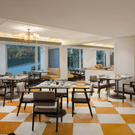 Bright hotel bedroom featuring floral linens, wooden paneling, a desk area, and a balcony with a scenic river view.