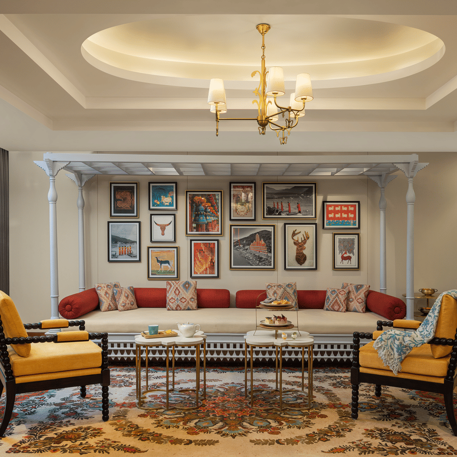 Traditional Indian-style daybed (diwan) seating area featuring red bolsters and a vibrant gallery wall of local art.