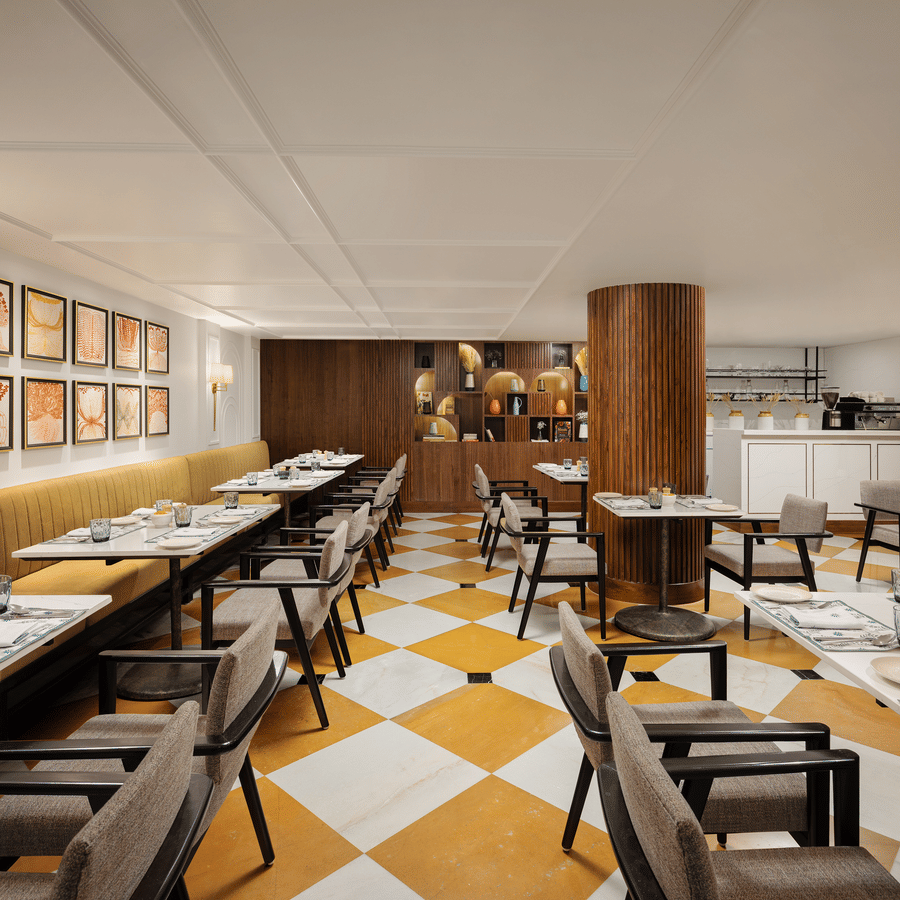 Modern restaurant interior with yellow banquette seating, gallery wall art, and a fluted wood pillar.