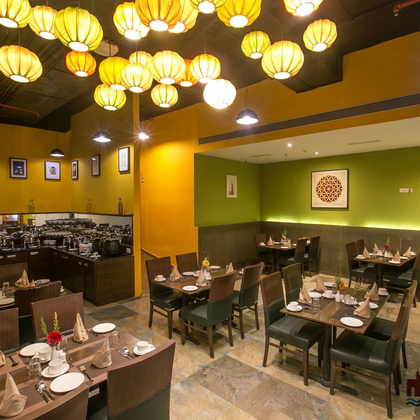 Hotel restaurant with colorful hanging lamps, art-decorated walls, wooden tables, and buffet area.
