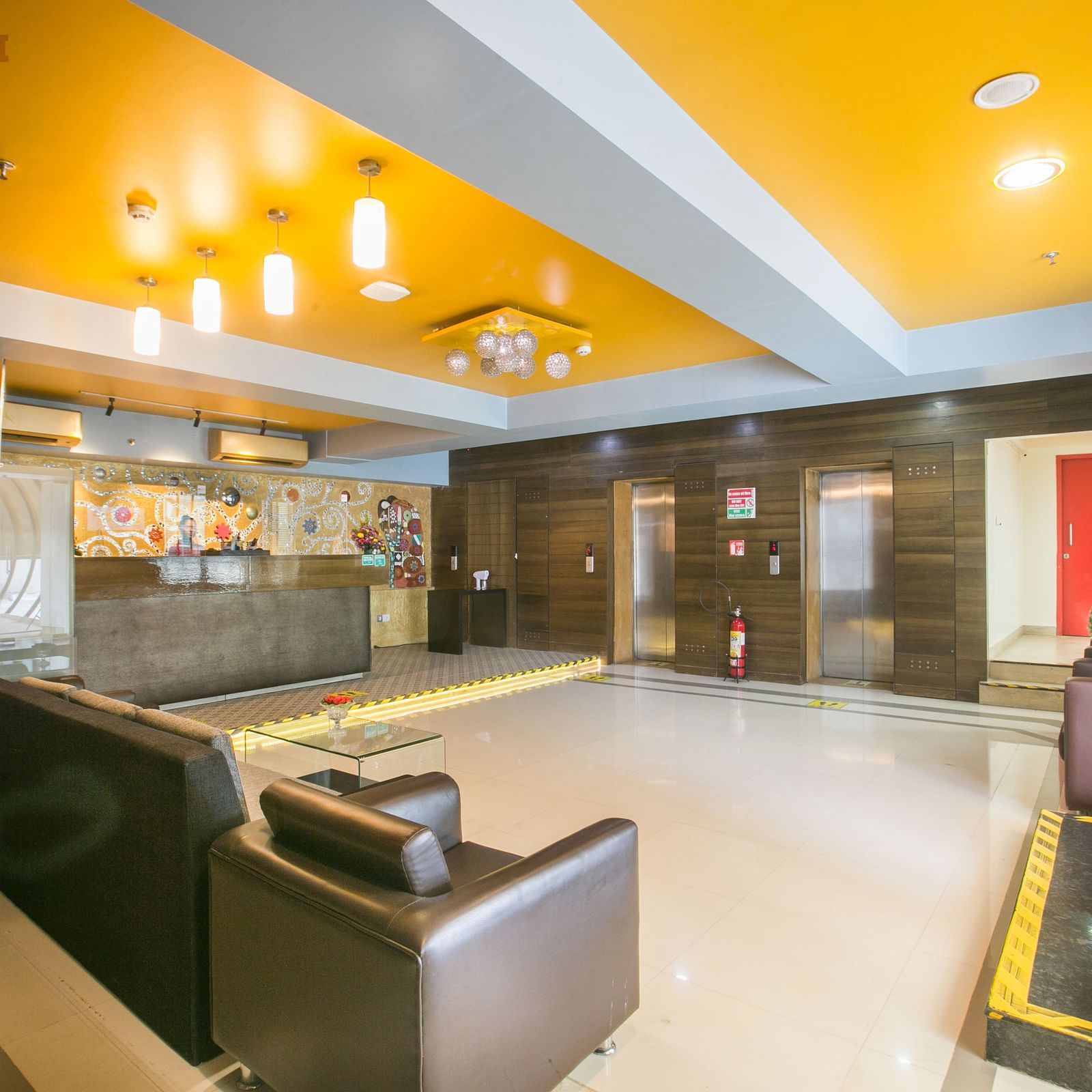 Spacious lobby with bright lighting, modern furniture, a vibrant yellow ceiling, and elevators.