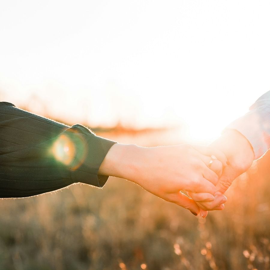 alt-text Two persons holding hands, during the golden hour, while walking through a field.