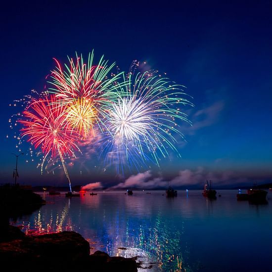 An overview of the night sky with firecrackers bursting and the lake being illuminated