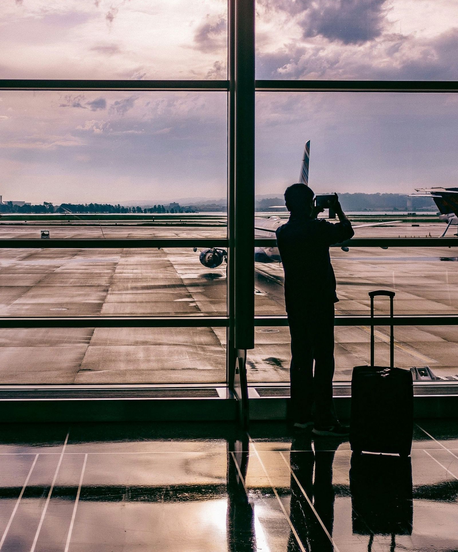 Silhouette of a person standing by a large window overlooking an airport runway.
