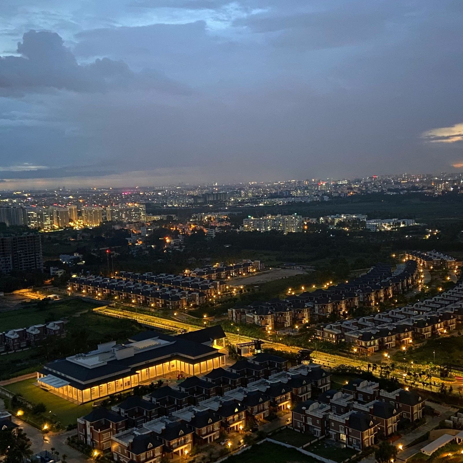 Cityscape at dusk with illuminated buildings and a curved road.