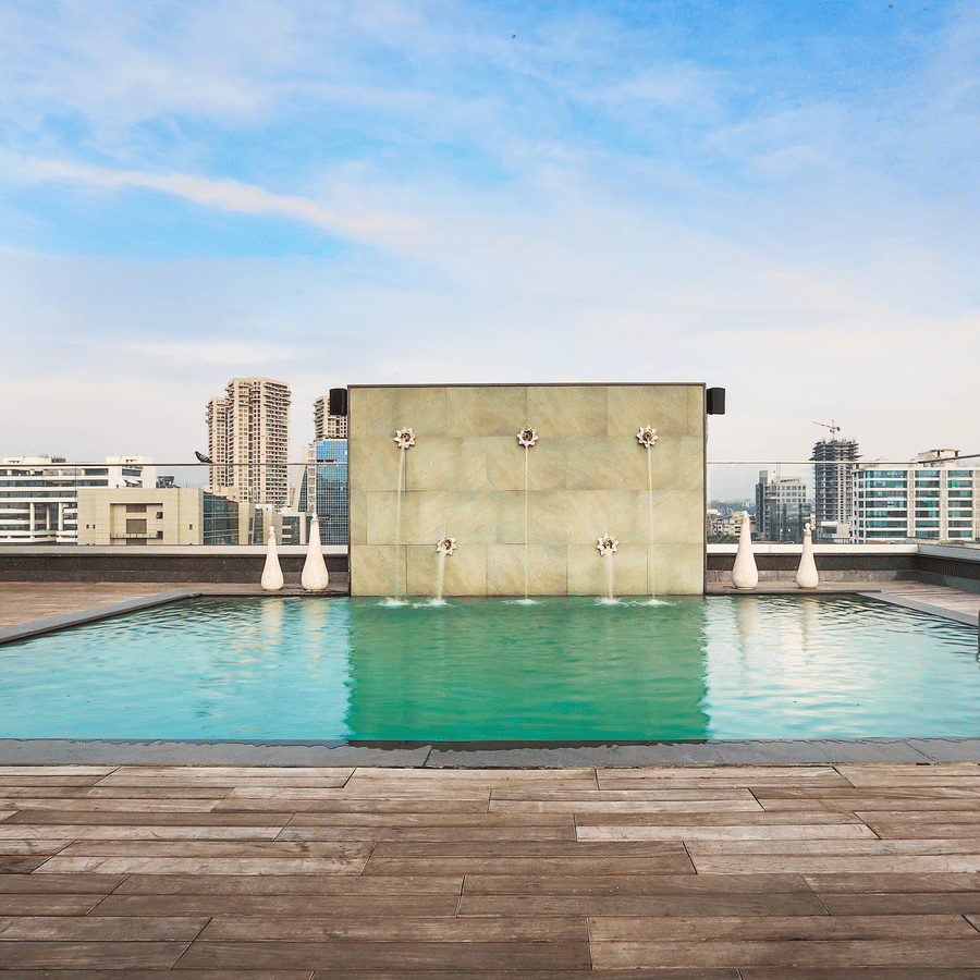 Rooftop swimming pool with clear blue water and a city skyline view under a bright sky.