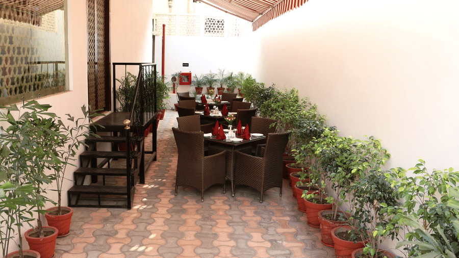 An outdoor seating area at Comfort Inn Sapphire by Eastlynn Collections, Jaipur, with tables, chairs, potted plants, and a red and white striped awning.