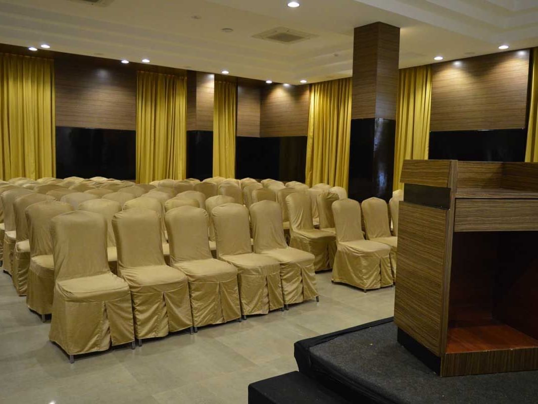A large banquet hall at The Royal Comfort, set up for a conference or event with rows of chairs facing a stage with a podium, all under warm lighting.