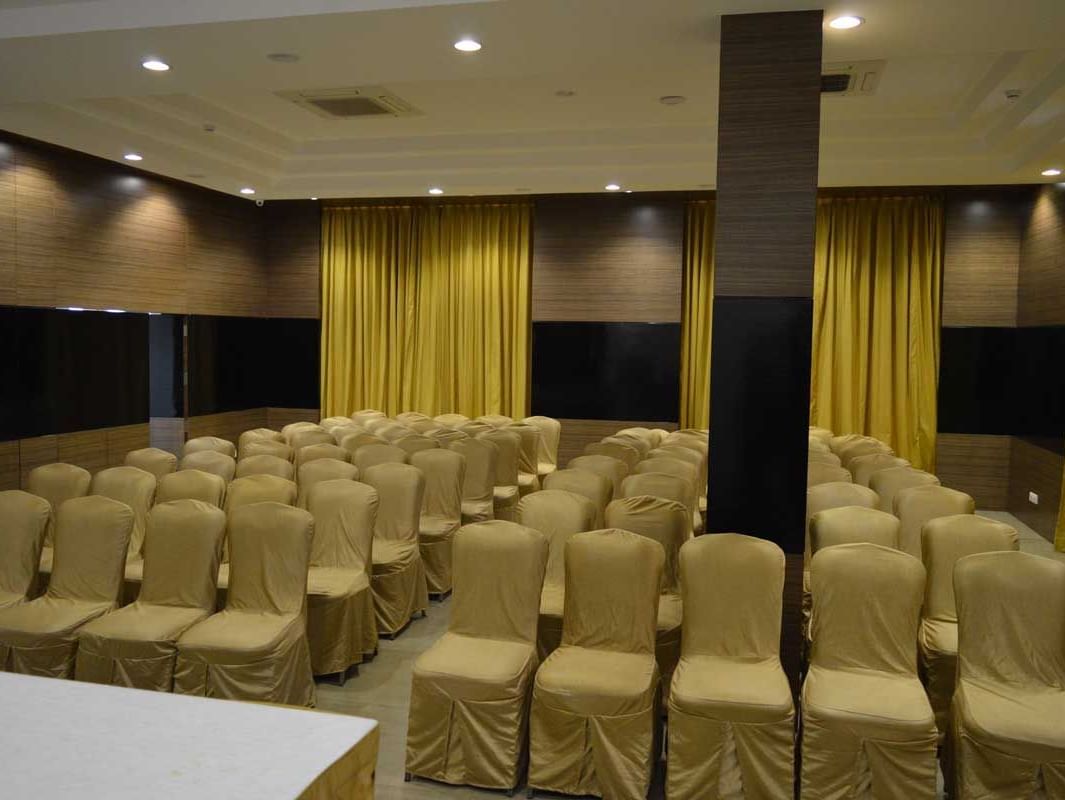 A large banquet hall at The Royal Comfort, set up for a conference or event with rows of chairs facing a stage with a podium, all under warm lighting.