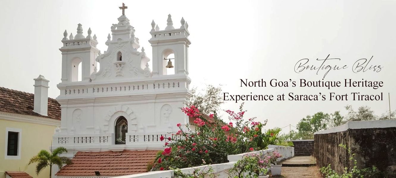 White heritage church with baroque design, framed by blooming red flowers.