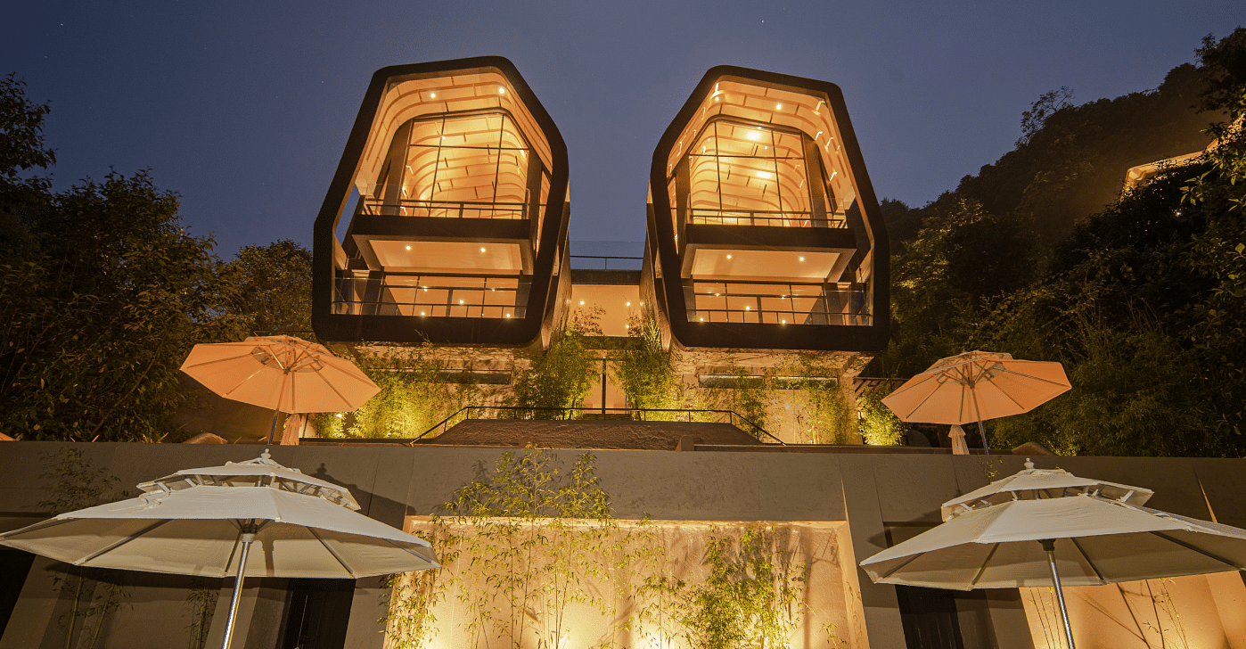 A front view of two individual beautifully lighted villas | A bedroom with large window giving a view of a sitting area on the deck | Kavya Resort and Spa, Nagarkot