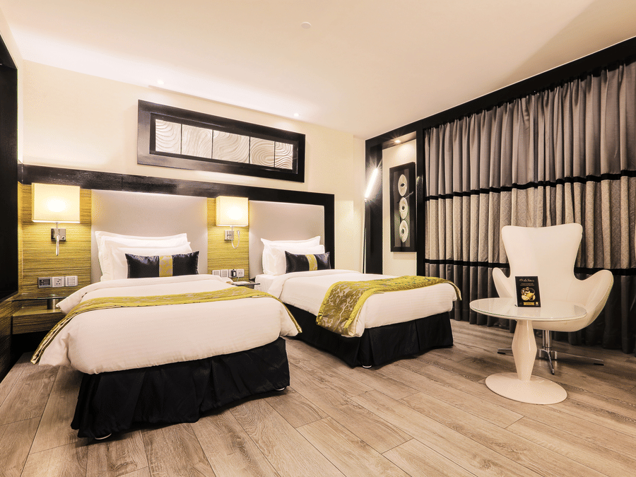 Executive Twin Room at The Empresa Hotel featuring two similar looking bed, and a chair with centre table.