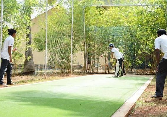 Two people playing a sport on a field, outdoor setting with trees in the background - Shreyas Retreat
