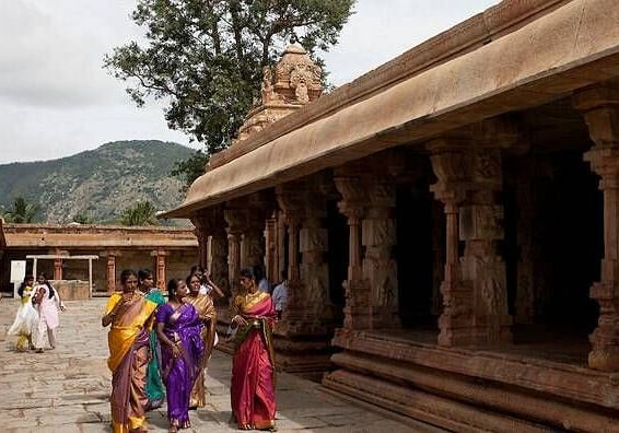 A stone temple structure with people walking along a colonnaded walkway.