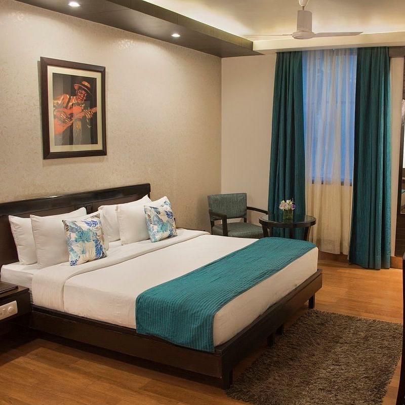 Modern hotel room at Rockland Hotels, New Delhi, featuring a plush bed, work desk, cosy seating, and elegant teal accents.