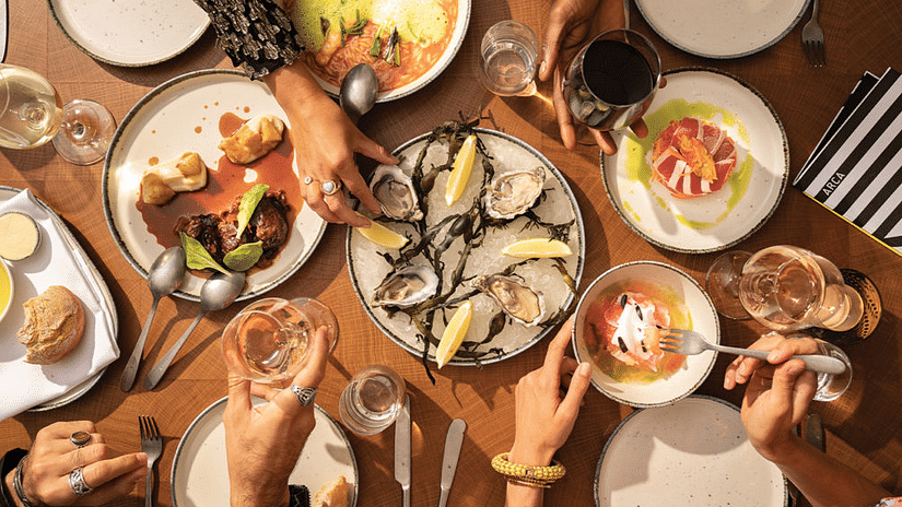An image of  a dining table where various dishes are kept including sea foods which people are tasting - Pride Hotel Chennai