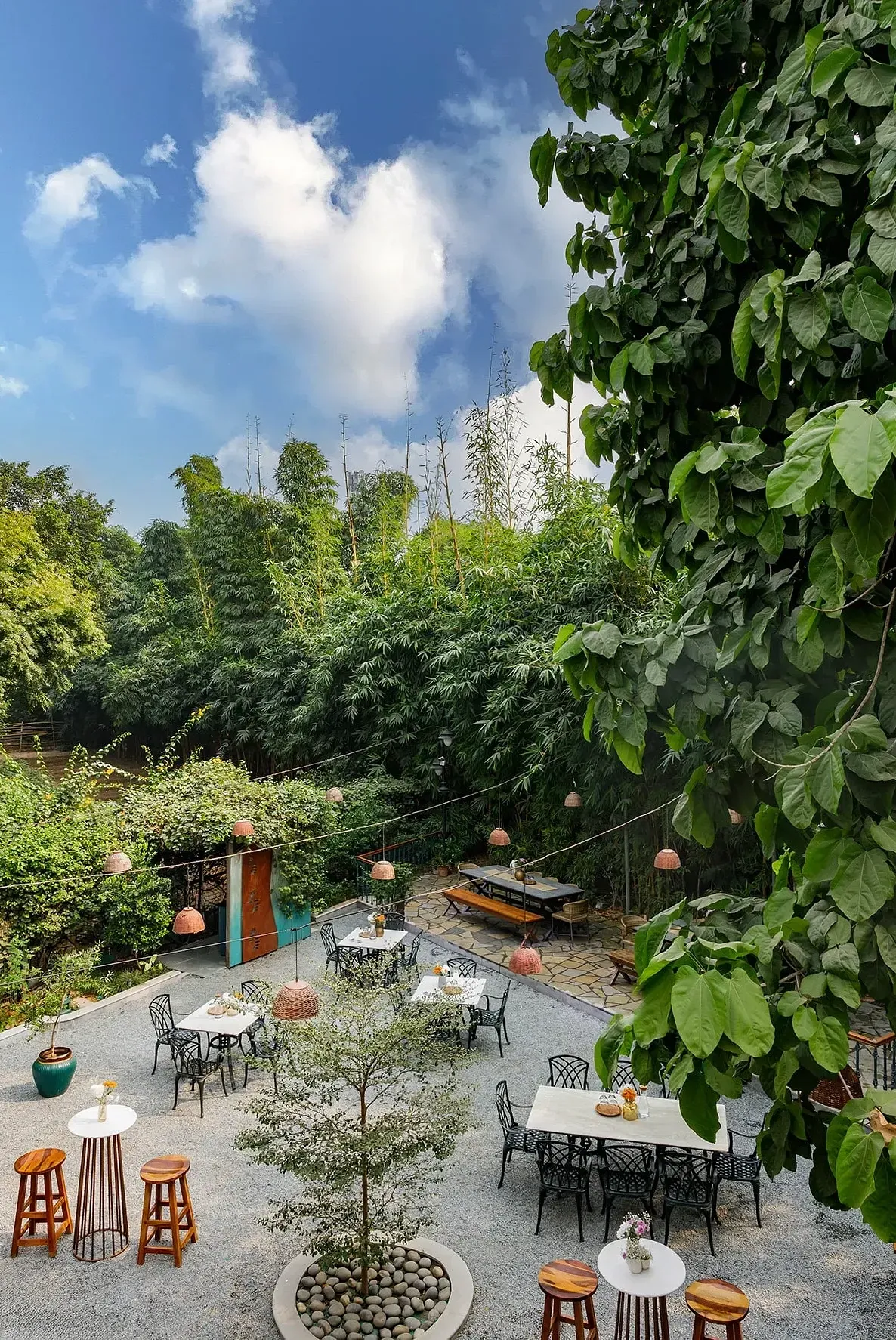 View of Karma Chalets's open-air seating area with round tables, chairs, and trees surrounding the space.