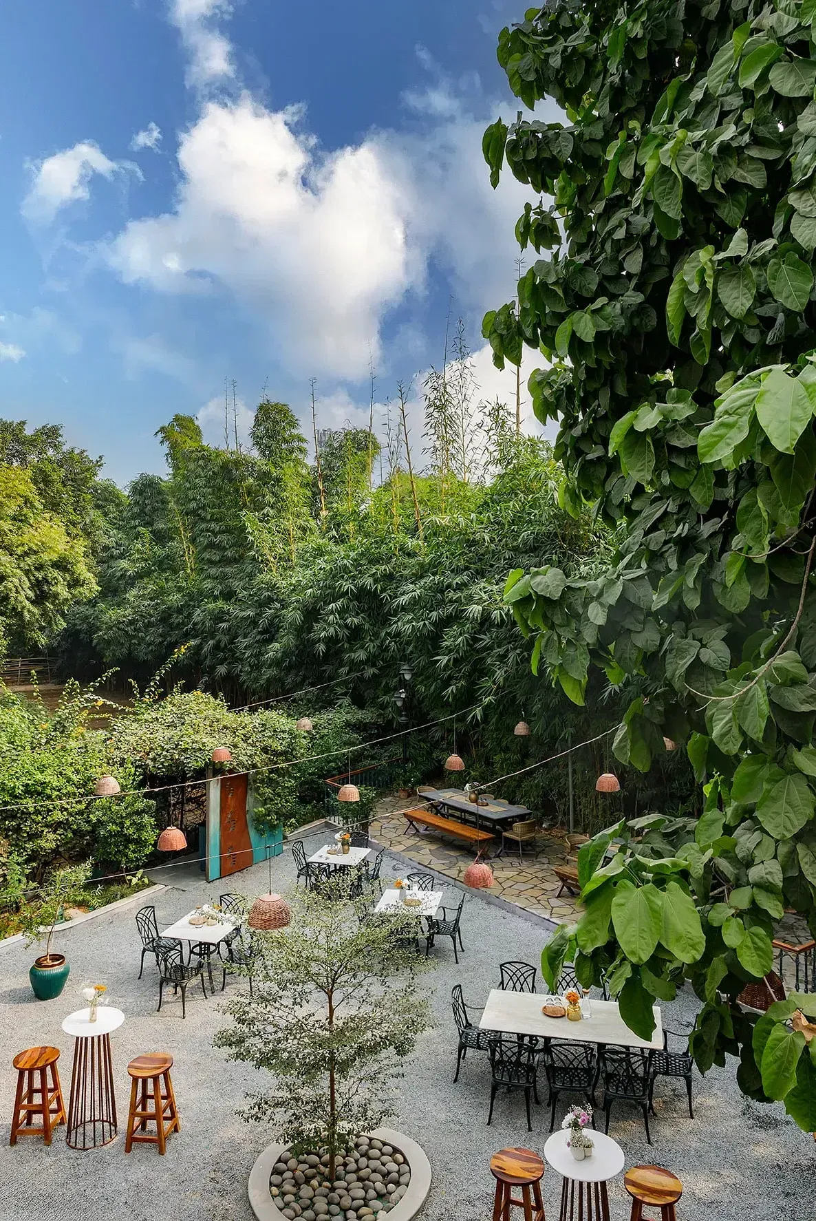 View of Karma Chalets's open-air seating area with round tables, chairs, and trees surrounding the space.