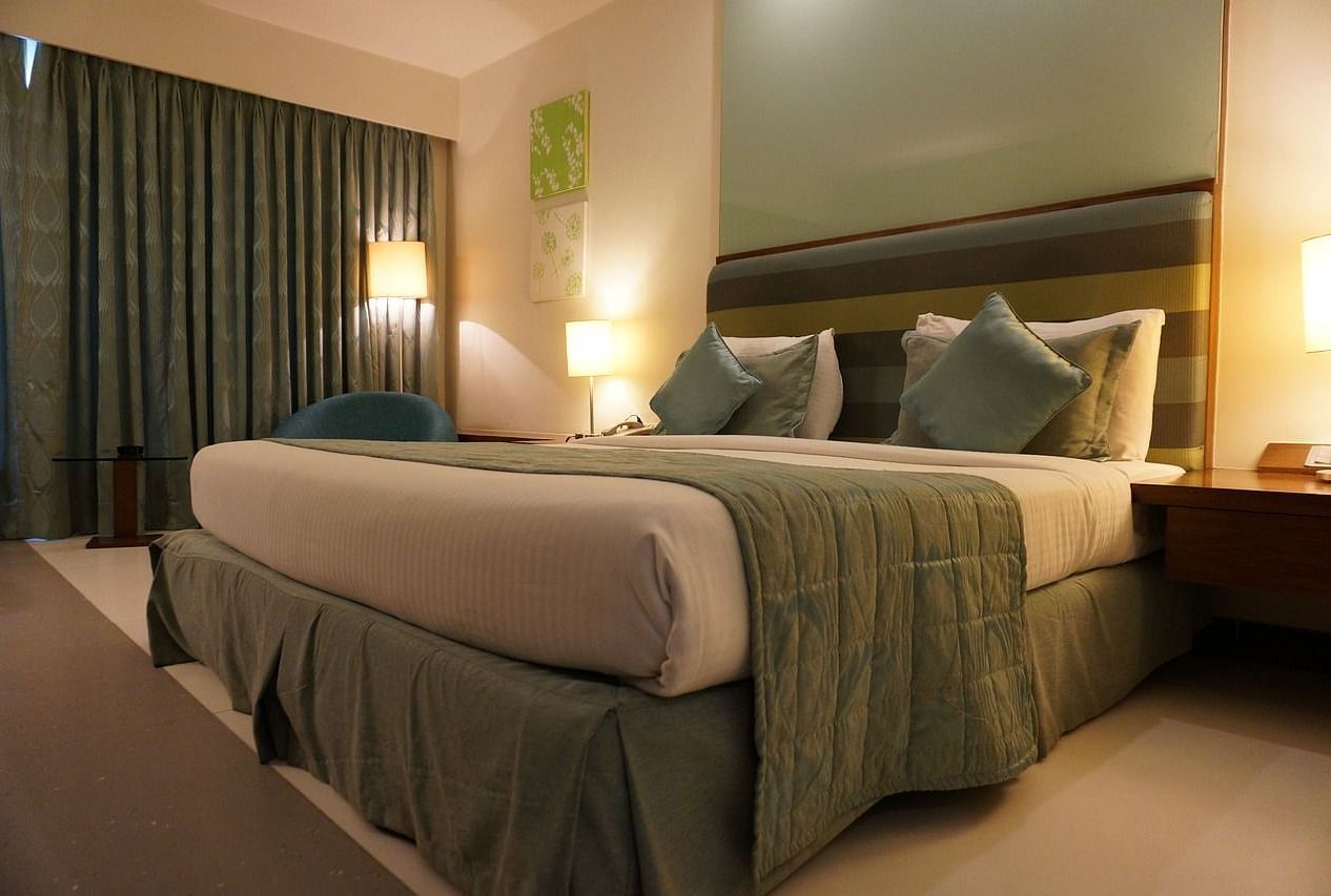 A double bed with pillows and cushions kept neatly against the head board of the bed in a warmly lit room.