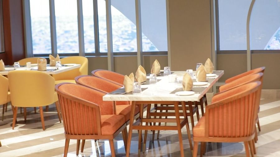 Sunlit dining room with large windows, orange upholstered chairs, and neatly set tables - Serene Sarovar Premiere Hargeisa