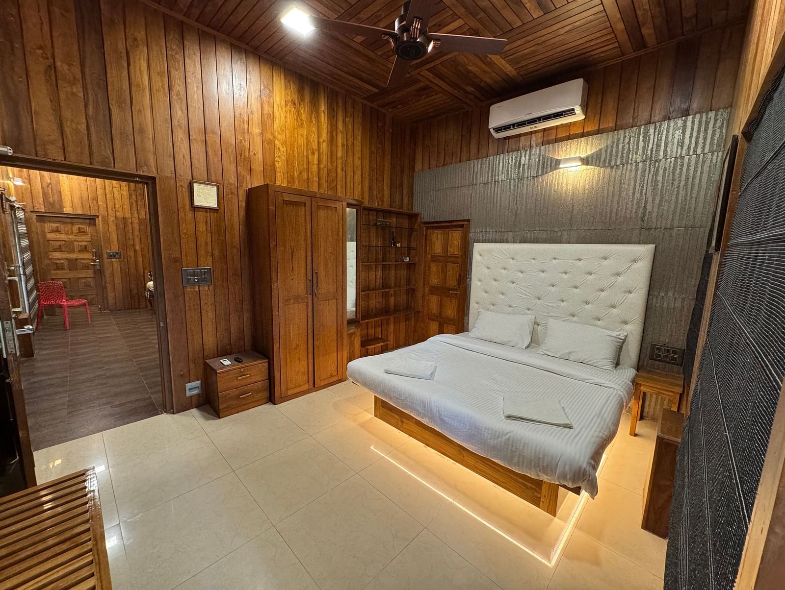A bedroom with rich wooden walls and ceiling, a platform bed with a white tufted headboard, and a ceiling fan.