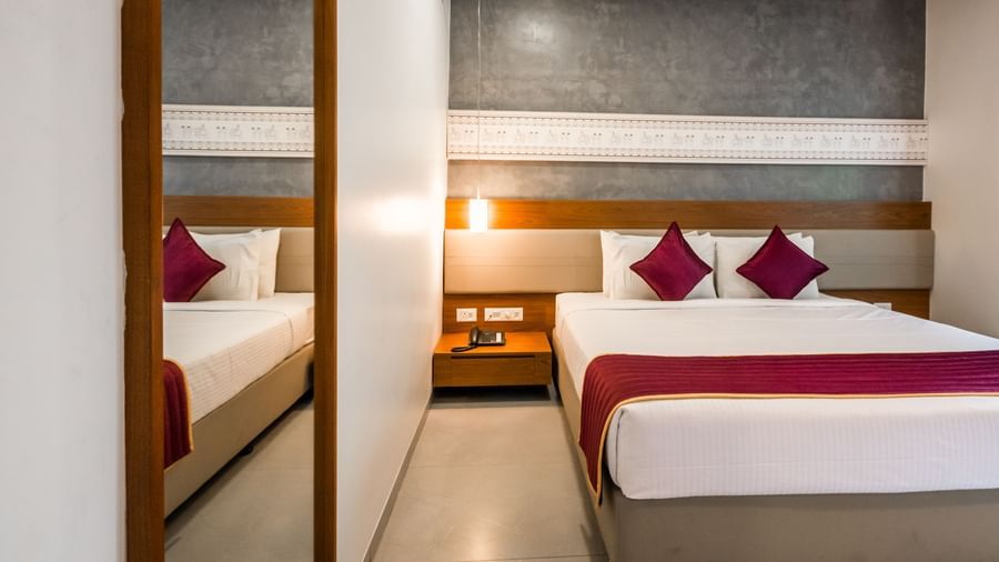 A comfortable hotel bed with a red runner and multiple pillows, set against a textured wall at Shilton Dee Cee.
