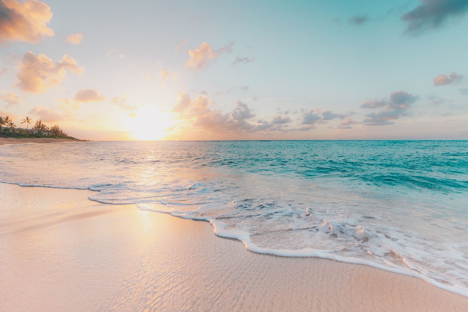 An overview of a beach with waves overlapping and the sun setting in the background - Getaways from Kochi