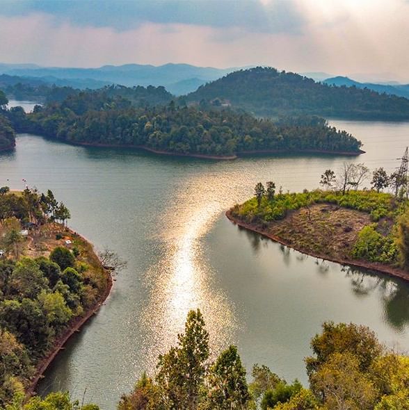 A view of a wide river with forested islands and hills under a partly cloudy sky near Polo Resort Cherrapunjee.