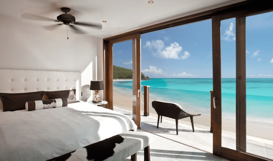 A spacious bedroom with a large bed opens up to a stunning ocean view through expansive glass doors.