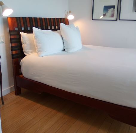 Bed with white linens and wooden headboard at Casa Morada, shown from a side angle.