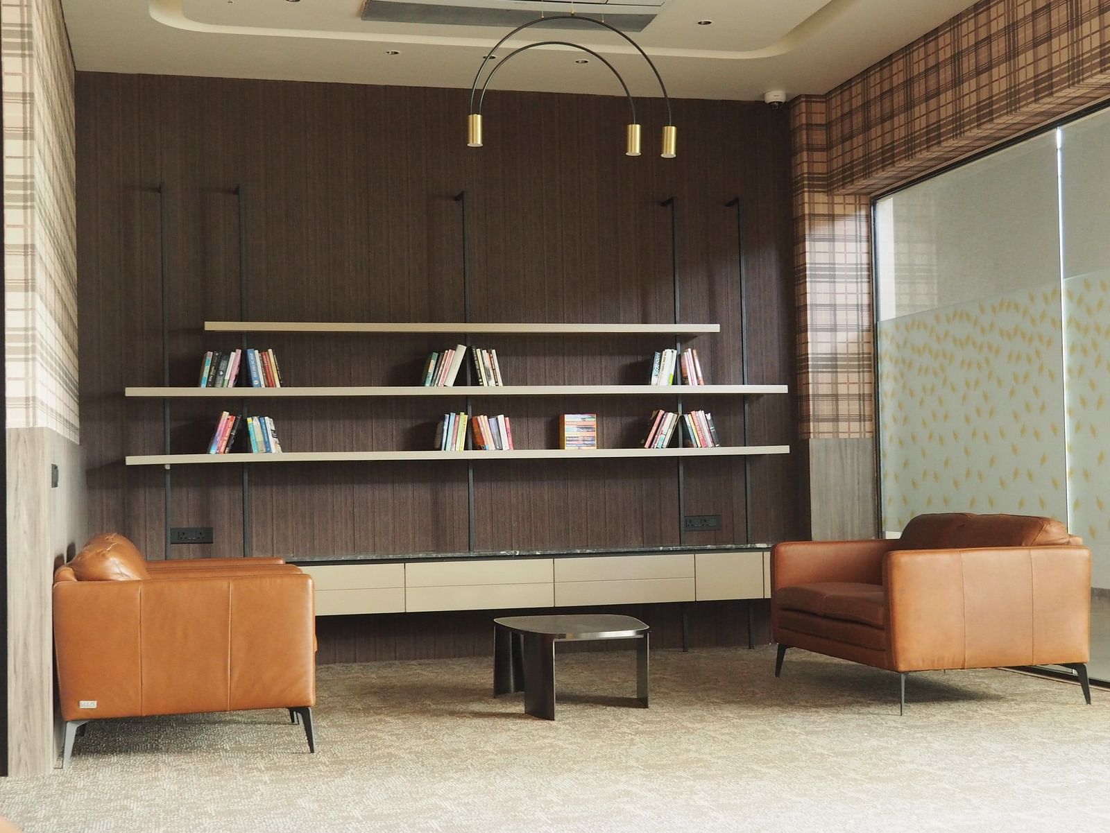A lounge area with armchairs and shelves, separated by a glass partition - Club Charholi, Pune 