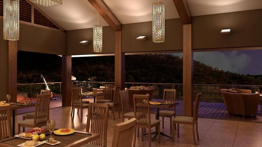 A restaurant with wooden tables and chairs, pendant lights, and an open wall leading to an outdoor area with a view of the hills - Gaurav Lords Resort Shrivardhan.