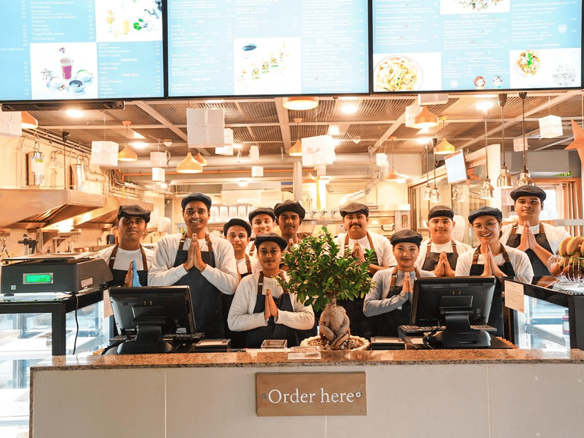 A quick service dining counter at Falaknuma restaurant with digital menu screens, front-facing order counter, staff lined up behind the counter, and kitchen area visible at Clarks Avadh, Lucknow.