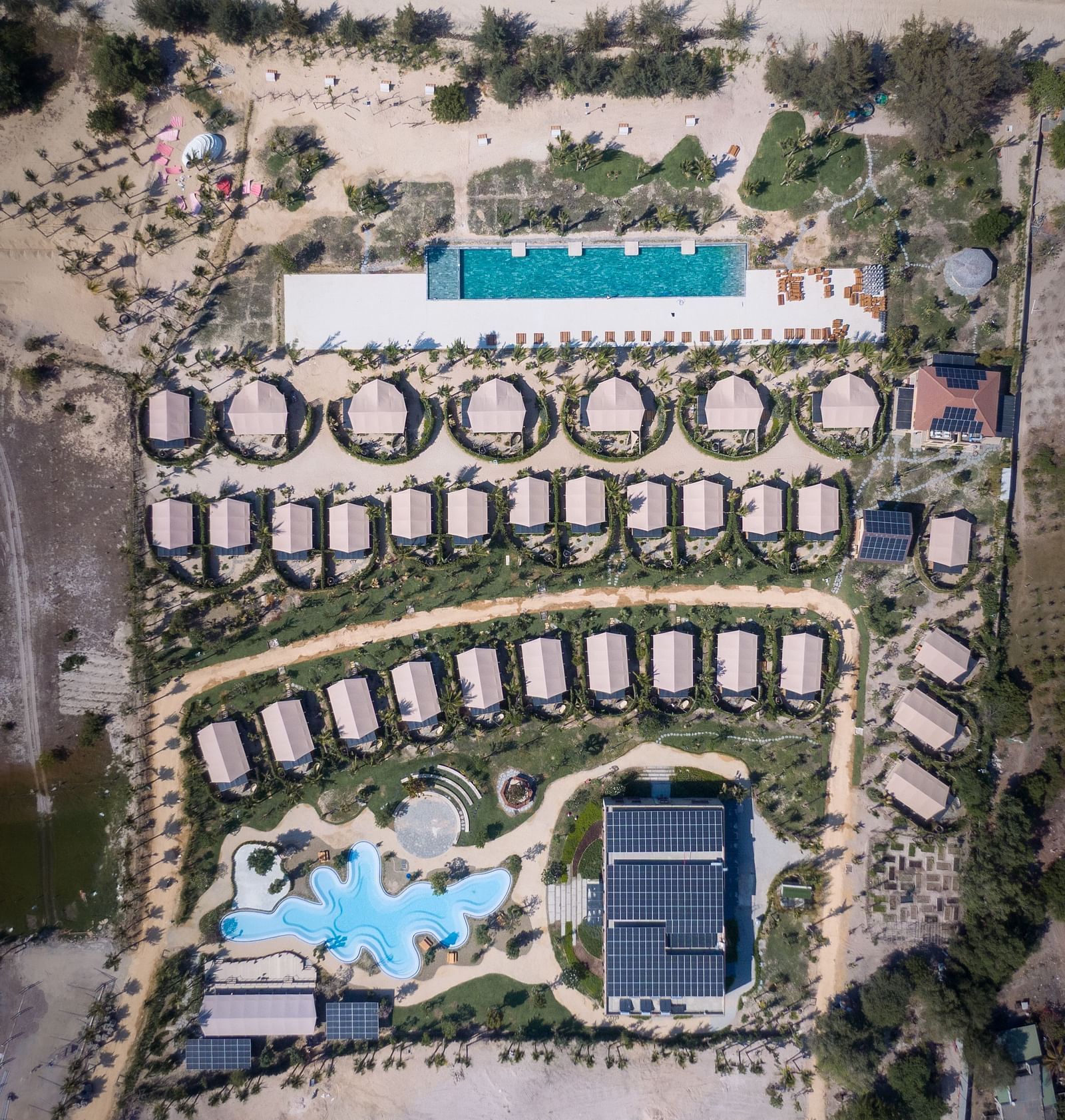 WoCAL Retreat Ke Ga featuring numerous circular bungalows, multiple swimming pools, and manicured green spaces nestled in a dry, coastal landscape.