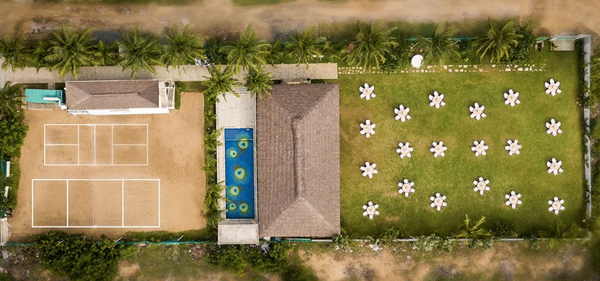 An aerial view of Grande Bay Resort & Spa, Mamallapuram, featuring a lawn setup for events on one side and a swimming pool and playground on the other side.
