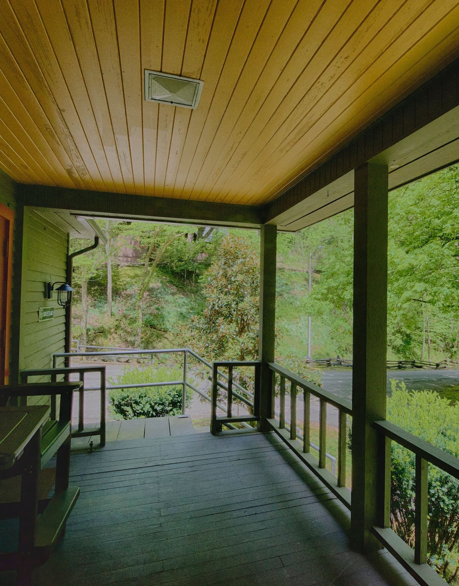a beautiful wooden porch with hand railings featuring wooden chairs overlooking the serene lush green views of the forest and the trees - Historic Tapoco Lodge