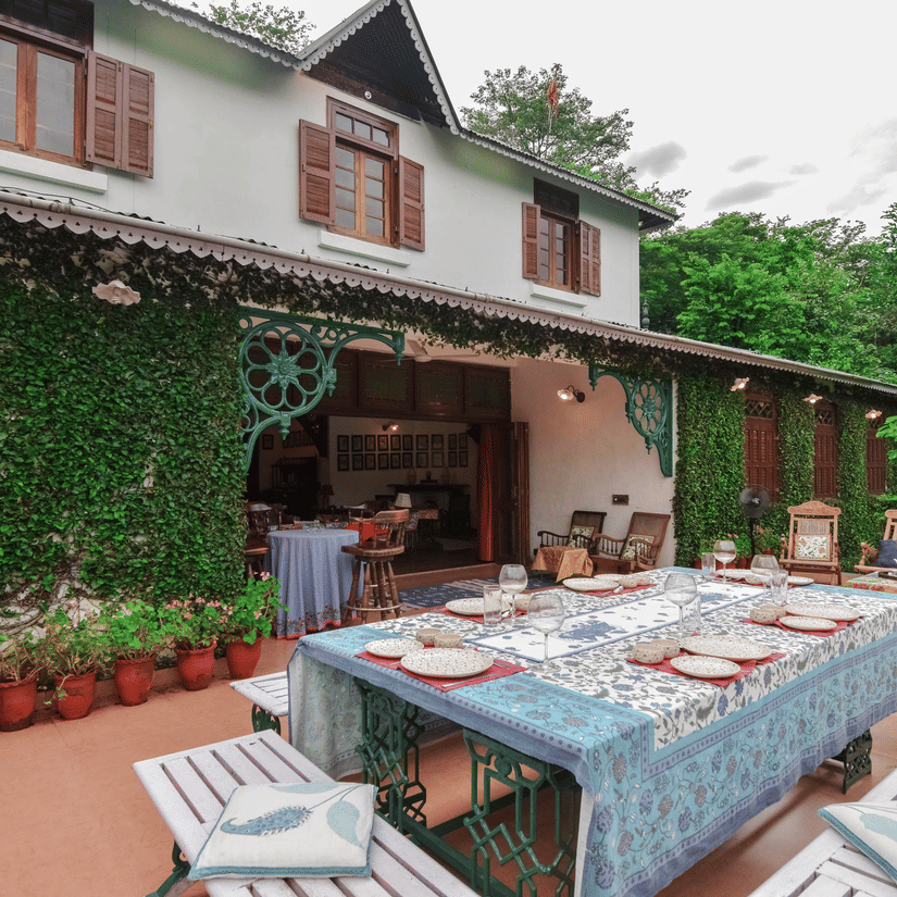 A dining table set outdoors with colourful linens and a view of the surrounding hills with greenery all around at Shaheen Bagh.