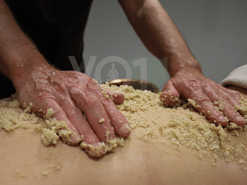 A therapist's hands spreading warm medicated rice paste across a guest's back