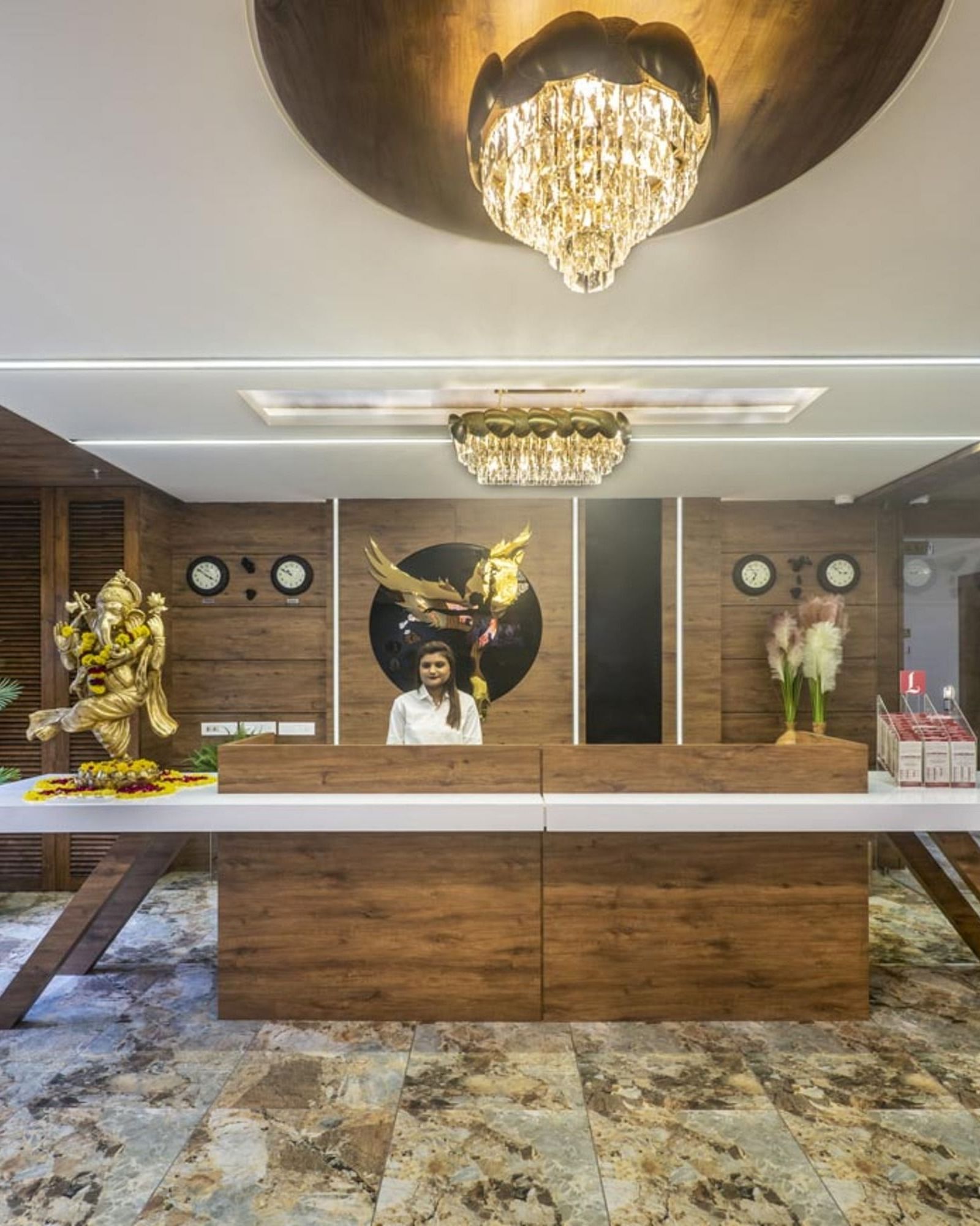 A well-lit hotel reception area with a wooden front desk and seating area towards the side at Angel Lords Eco Inn Amreli.