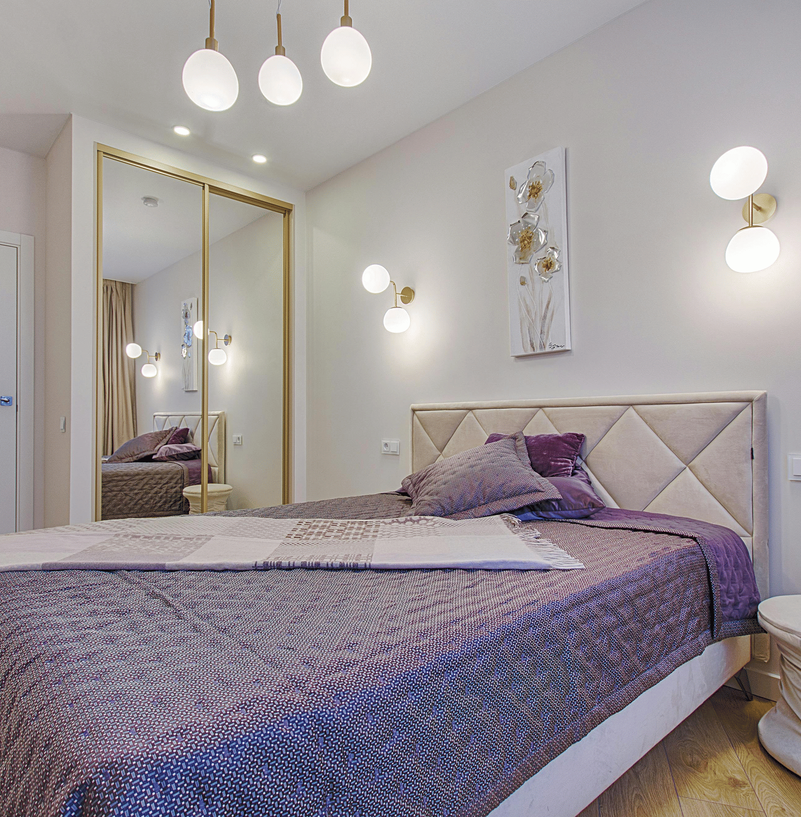 A minimalist bedroom with a quilted purple bedspread, a diamond tufted headboard, and mirrored wardrobe doors.