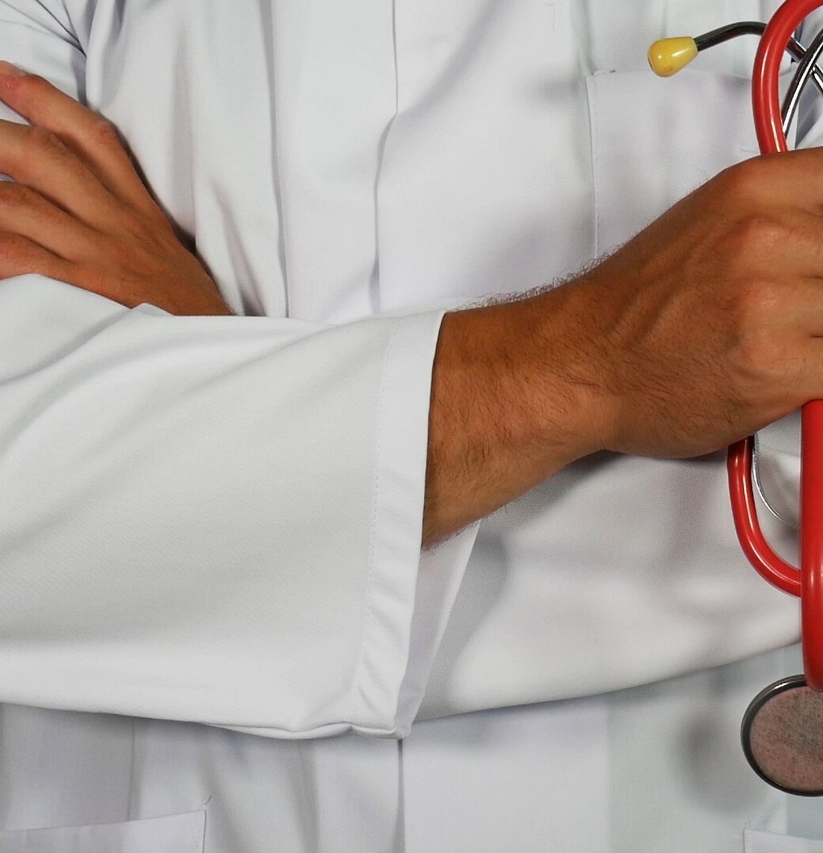 A doctor with folded hands, holding a stethoscope and wearing a white gown