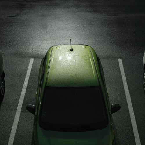 An aerial view of a green car parked between two white cars in a night-time parking lot