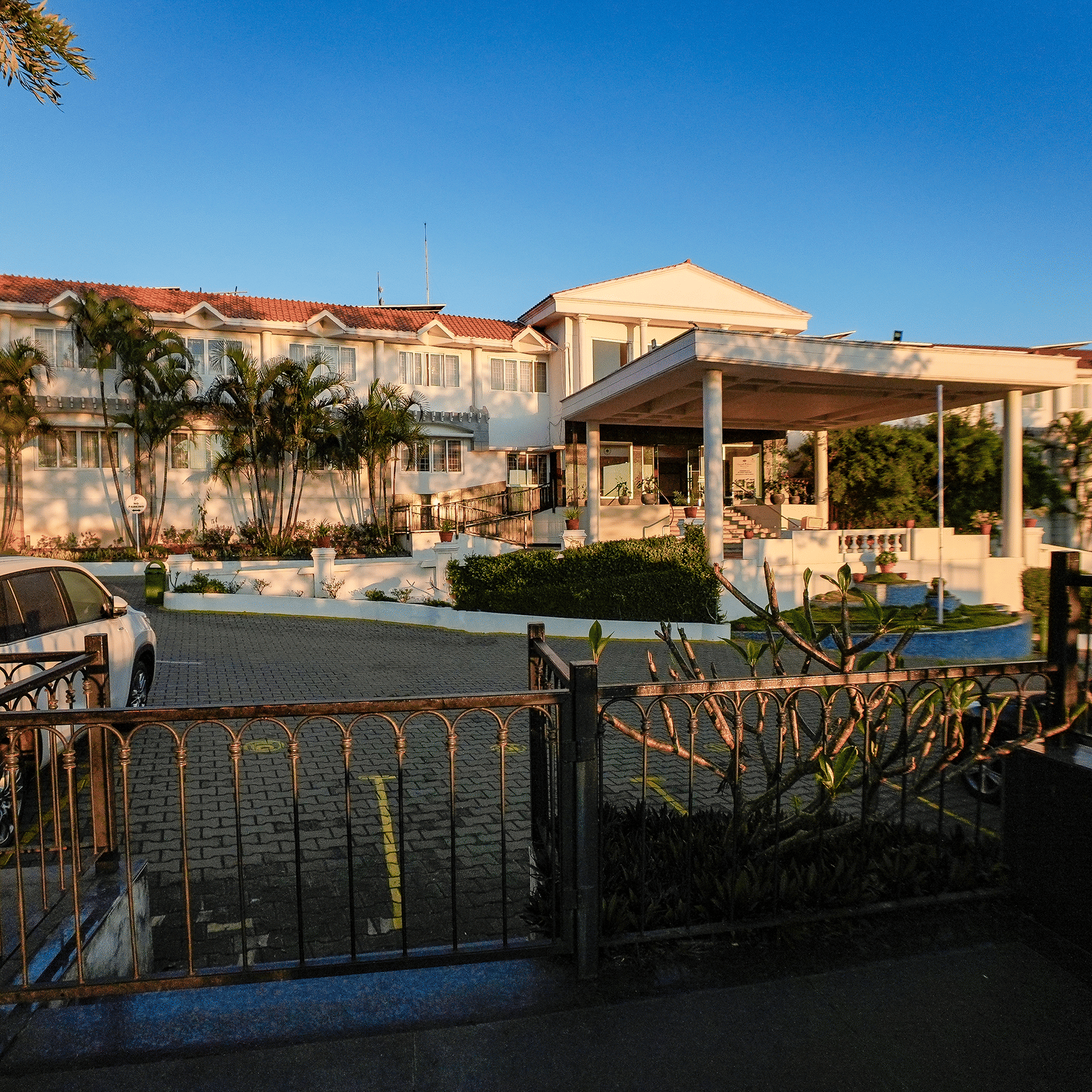 Outdoor restaurant seating area at Grand Palace, Yercaud facing hotel building, railing, garden and patio visible under open sky.