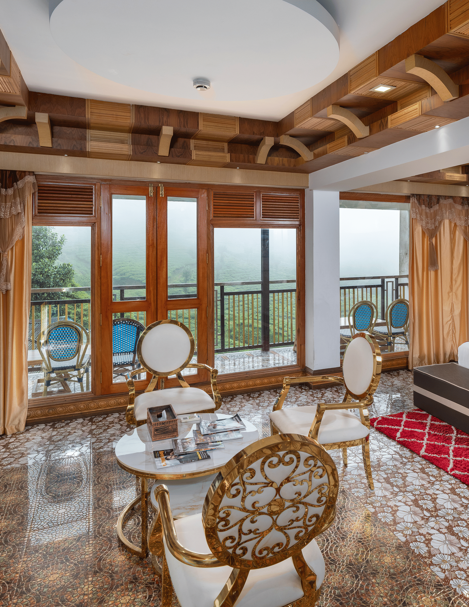 The expansive bedroom of the Presidential Suite at Parakkat Nature Hotel and Resorts, Munnar, featuring a large bed, decorative wooden-beam ceilings, a seating area with a table, and glass doors opening to a scenic view.