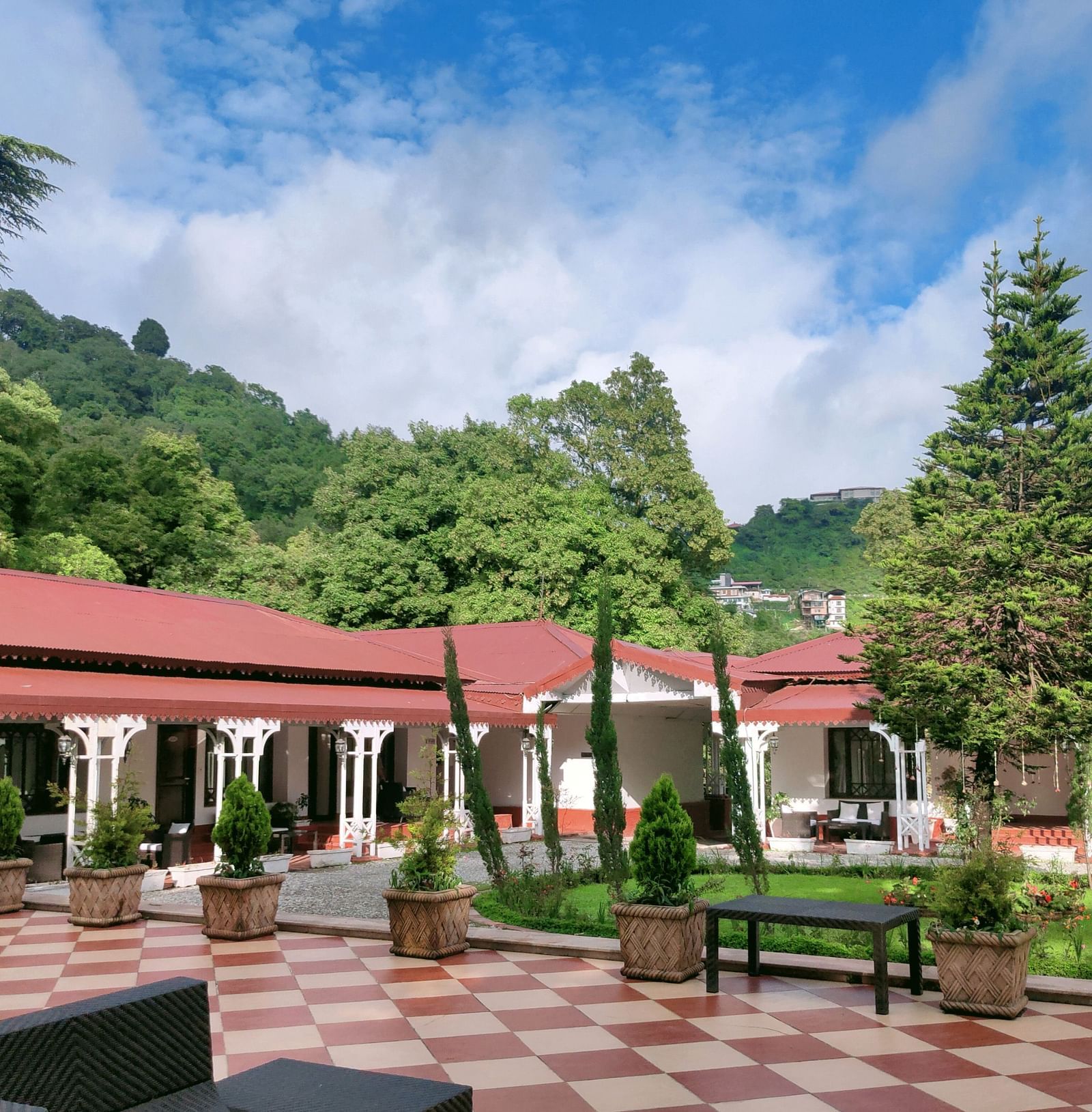 Facade view of The Claridges Nabha Residence in Mussoorie with a backdrop of a lush green forest with a blue sky with clouds