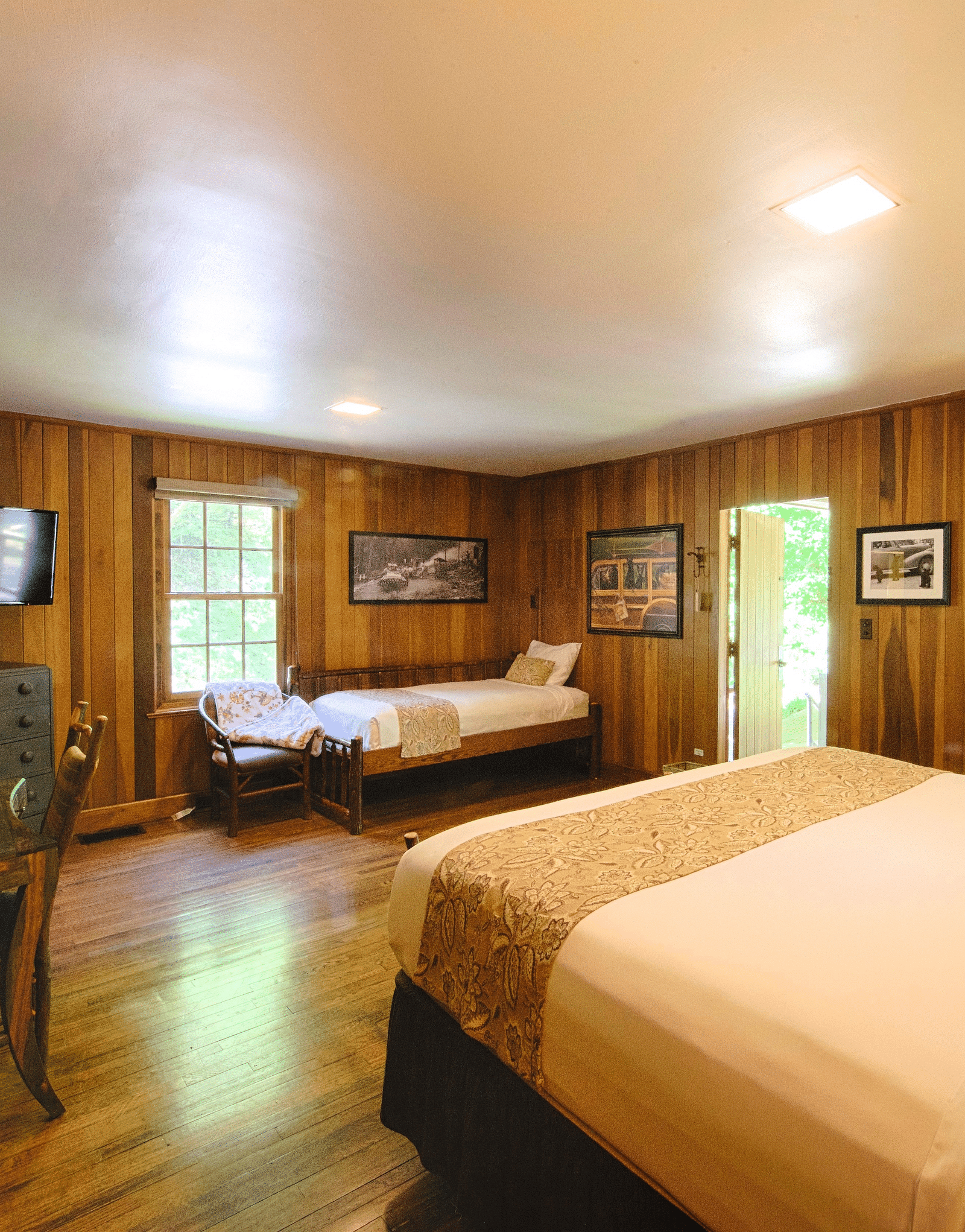 corner view image of a bedroom decorated with small photo frames on the wooden wall with a double and a single bed in the room - Historic Tapoco Lodge