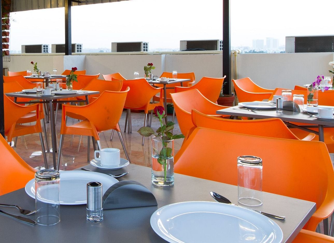 An outdoor dining space under a canopy offers numerous tables with bright orange seating at Sanctum Suites Whitefield, Bangalore.