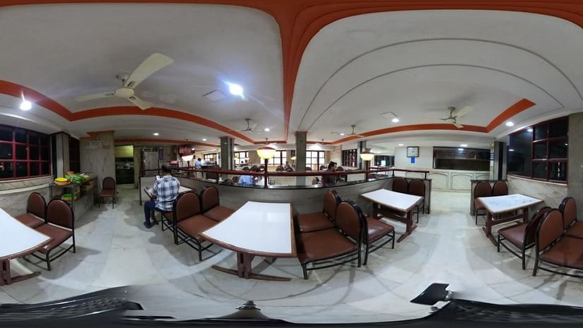 Dining area at Hotel Swagath, Bangalore with neatly arranged tables, cushioned chairs, and arched red ceiling design.