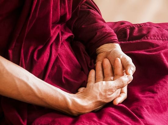 A serene moment of stillness captured in a close-up of meditative hands resting gently on maroon robes—symbolising mindfulness, inner peace, and the healing power of silence in spiritual wellness practices.