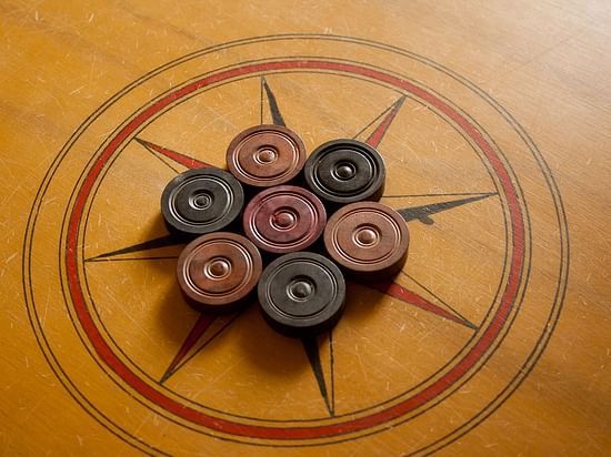 A carrom board with carrom pieces set up for a game